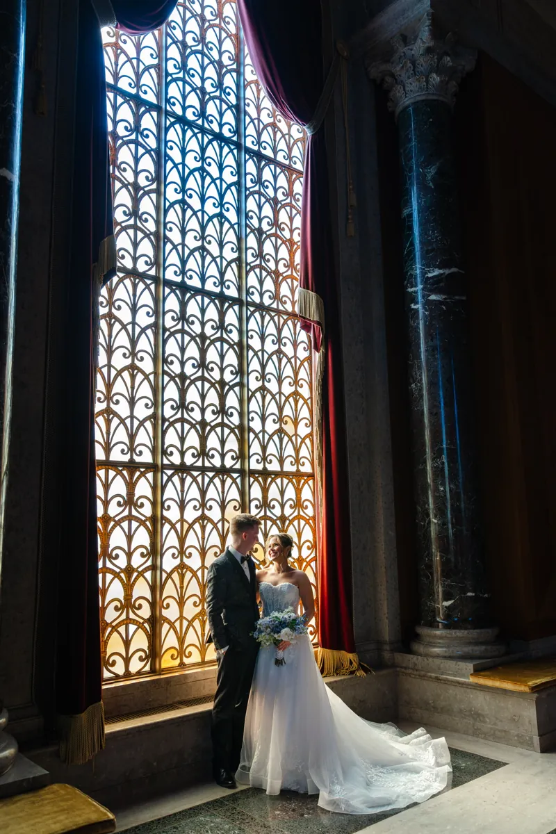 Pearson and Emma on their wedding day, standing by a tall ornate gold window
